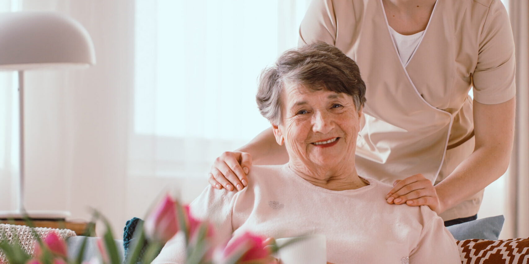Smiling elderly woman drinking tea with her caregiver in the retirement home