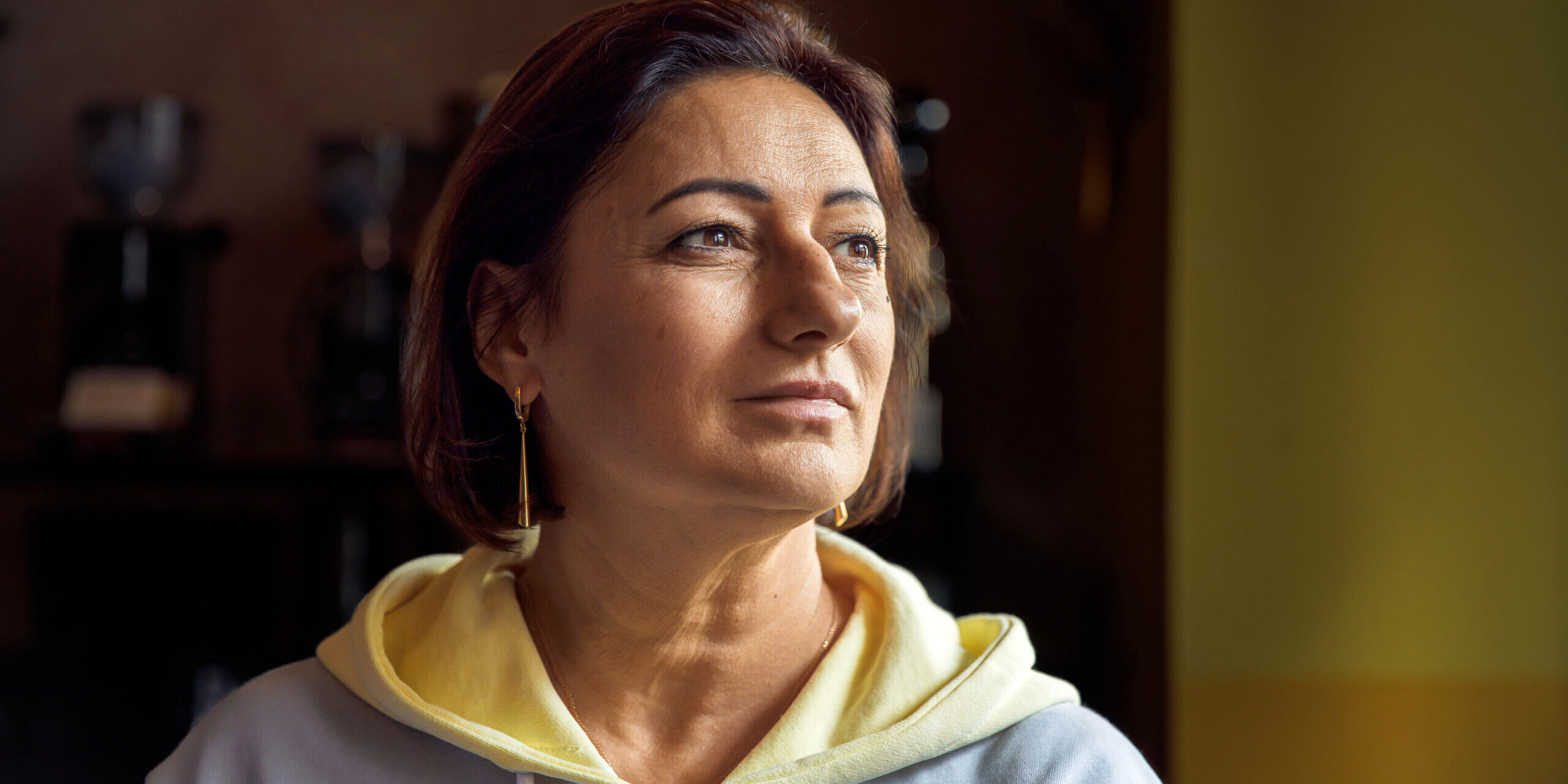 Thoughtful woman in casual hoodie sitting indoors with warm lighting