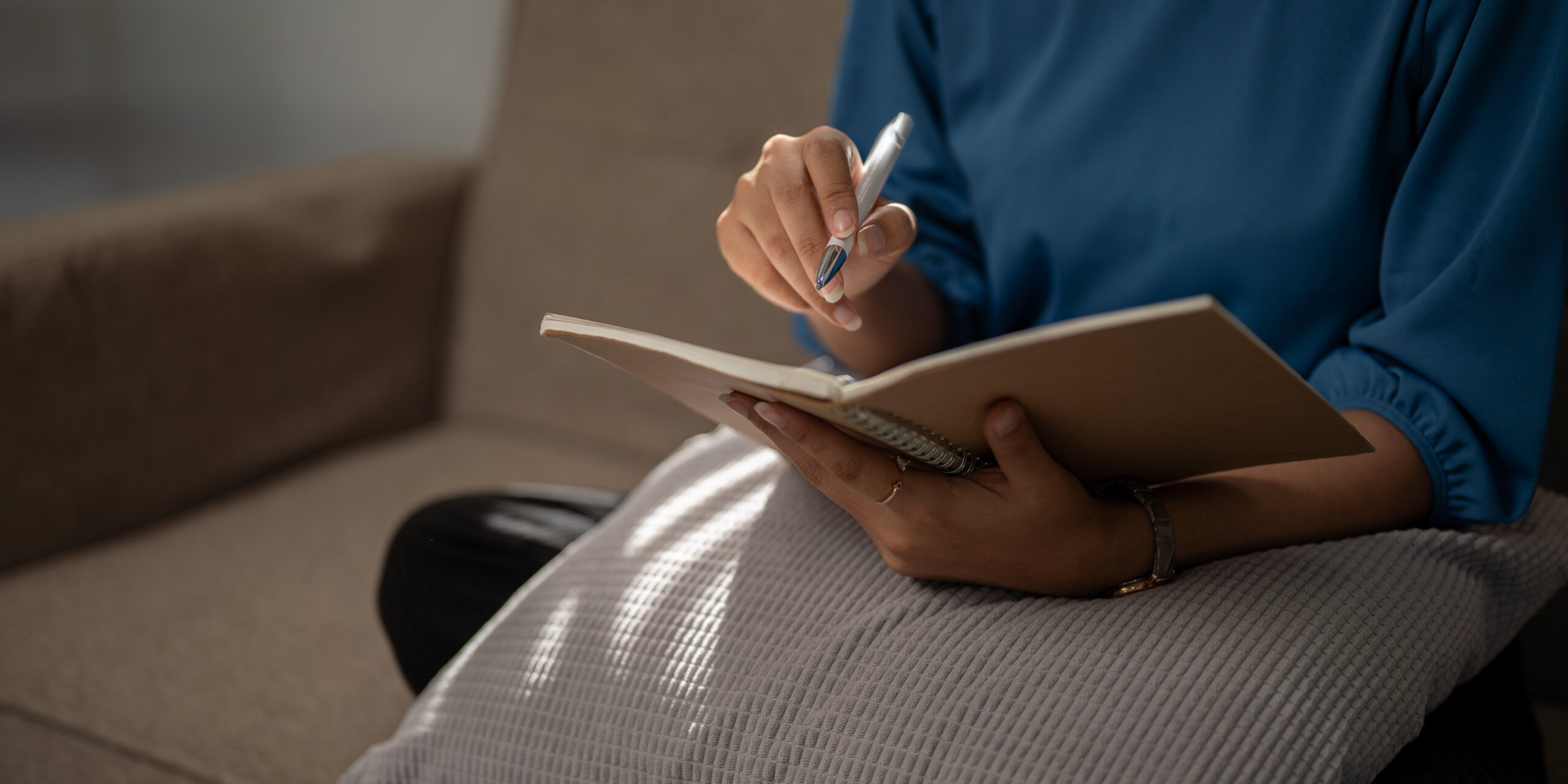 Close-up image of a woman in casual clothes is keeping her diary or taking notes on a notebook.